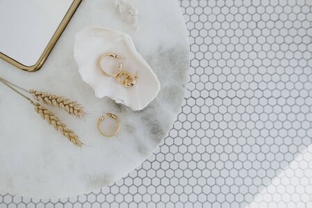 Minimal fashion composition with golden earrings in seashell on marble table with mirror and wheat stalks. Flat lay, top view bijouterie / jewelry concept on mosaic tile background.の写真素材
