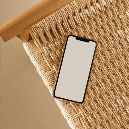 Blank screen smartphone and wicker bench on beige background. Flat lay, top view empty copy space mockup templateの写真素材