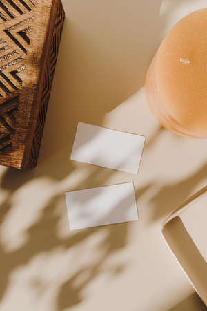 Blank paper sheet cards with empty copy space, wooden casket and candle and floral sunlight shadows on beige background. Flat lay, top view business mock up template.の写真素材