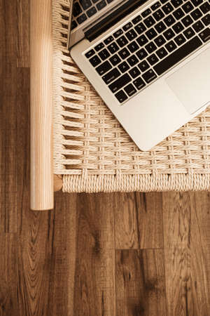 Laptop keyboard and wicker bench on wooden floor. Flat lay, top view home office workspace