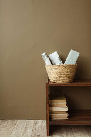 Handmade paper gift boxes in straw basket on wooden stand with books. Minimalist interior design concept.の写真素材