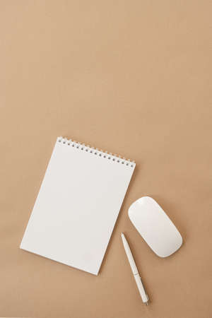 Flatlay of blank sheet spiral notebook, mouse, pen on pastel beige table. Flat lay, top view. Copy...