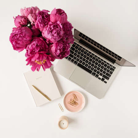 Laptop, beautiful pink peony tulip flowers bouquet and notebook on white table background. Flat lay, top view minimalist home office desk workspace.の写真素材