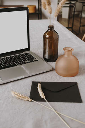 Blank display laptop, envelope, fluffy plants, rye / wheat ear stalks, decorations on gray washed linen cloth. Flat lay, top view minimalist home office desk workspace. Lifestyle blog composition.の写真素材