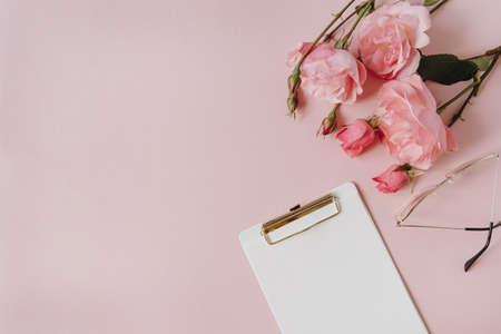 Blank paper sheet clipboard note pad, rose flowers bouquet, glasses on pink background. Minimal home...