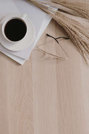 Flatlay of coffee cup, pampas grass, glasses, magazines on beige wooden background. Flat lay, top...