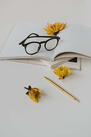 Minimalist home office desk workspace. Blank paper sheet notebook, glasses, yellow flower bud, stationery. Template for blog, social media, website. Bright work, business concept.の写真素材