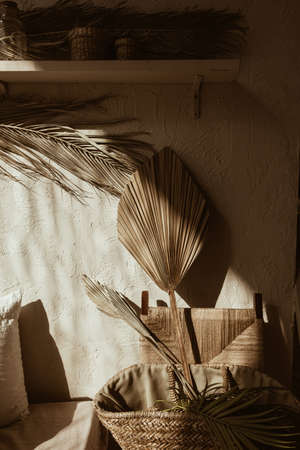 Modern boho style home interior design. Bohemian decorations on concrete wall. Dry palm leaf in straw bag. Warm sunlight shadows on the wall. Hygge concept.の写真素材