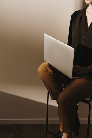 Aesthetic fashion composition with young pretty woman with laptop computer sitting on stool. Tan sunlight shadow on the wall.の写真素材