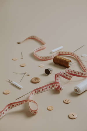 Sewing tools: buttons, spool, thimble, tape-measure on neutral beige background. Hobby, leisure...