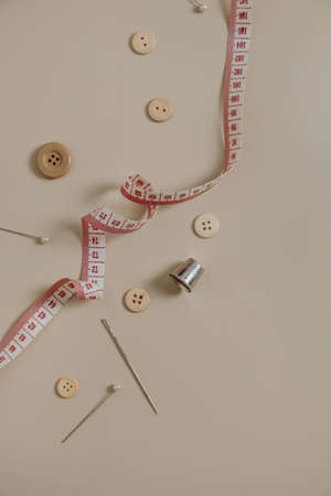 Sewing tools: buttons, spool, thimble, tape-measure, needles on neutral beige background.