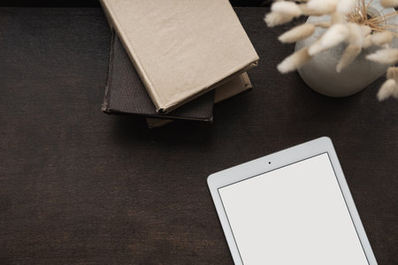 Flatlay of blank screen tablet, fluffy bunny rabbit tale grass on brown background. Office desk...