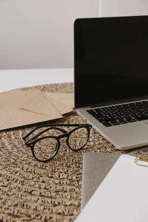Laptop, clipboard, envelope on rattan background. Aesthetic minimal freelancer, blogger home office workspace.の写真素材