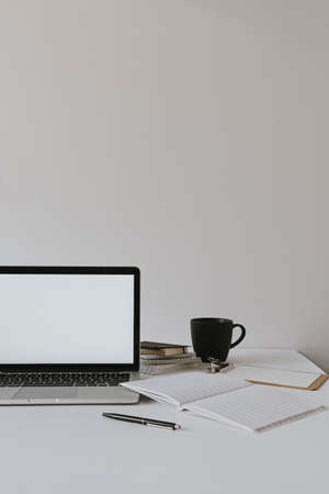 Minimalist home office desk workspace. Laptop with blank copy space mockup on table with coffee cup, paper sheet, stationery against white wall. Work, business background.の写真素材