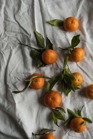 Raw oranges, mandarins fruits with green leaves on gray crumpled linen cloth. Healthy food concept. Flat lay, top view.の写真素材