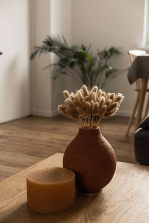 Candle, rabbit tail grass bouquet in clay pot on tableの写真素材