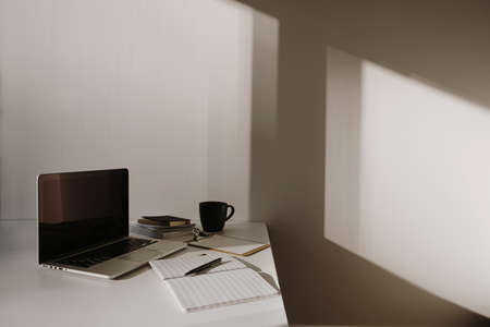 Minimalist home office desk workspace. Laptop on table with coffee cup, paper sheet, stationery...