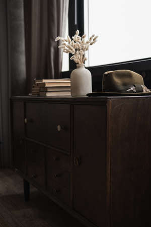 Rabbit bunny tail grass bouquet in pot, books stack, hat on table against windowの写真素材