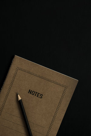 Craft notebook sheet, pencil, clips on black background. Flat lay, top view minimalist aesthetic lifestyle concept. Schedule list.の写真素材