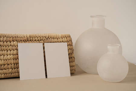 Blank paper sheet cards with mockup copy space, rattan casket, vase against neutral white wall. Minimal aesthetic business branding, blog, social media template backgroundの写真素材
