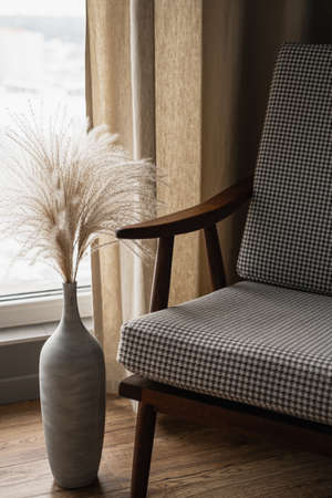 Mid-century retro chair and pampas grass bouquet in clay pot against window with curtains. Modern aesthetic minimalist home, living room interior design conceptの写真素材