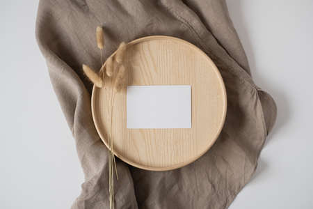 Flatlay of blank paper business card with mockup copy space and bunny tail on wooden tray on neutral beige blanket background. Aesthetic minimal business template for social media. Flat lay, top viewの写真素材