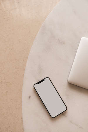 Blank screen mobile phone and laptop on marble table. Flat lay, top view minimalist blog, website, app template. Copy space mockup.の写真素材