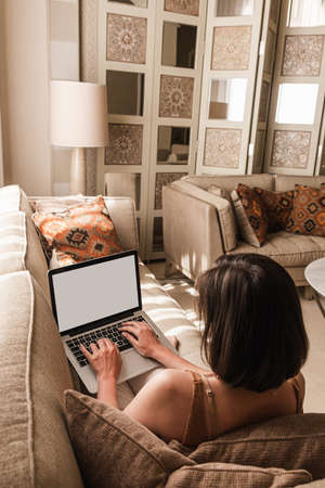 Young beautiful woman work on laptop computer with blank screen. Eastern traditional home interior design concept. Oriental style living room. Copy space mockup template backgroundの写真素材
