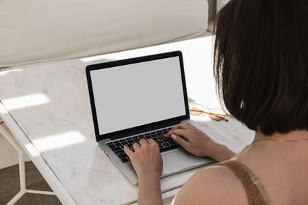 Young woman workin on laptop computer on marble table with sunlight shadows. Work at home concept. Girl boss, lady boss business composition for blog, web, social media. Blank mockup copy space screenの写真素材