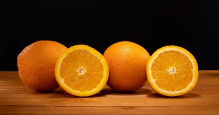 Fresh and juicy half and slice of orange fruit on a wooden table and black background.の写真素材