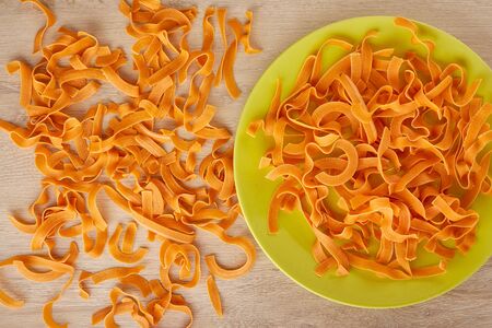 Raw orange pasta with tomatoes on a green plate, top viewの写真素材