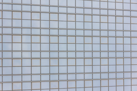 The glass facade of a tall building with the reflection of the blue skyの写真素材