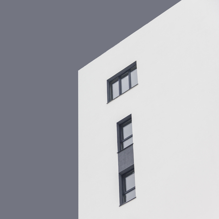 White apartment block with dark grey windows under abstract grey sky. Isolated. Quadrate photo. Bottom view. Concept: life, couple, family, kids, independence, abstract, minimalism.の写真素材