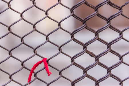 Rusty steel chain link or wire mesh as boundary wall. Red thread. There is still concrete block wall behind the mesh. Best securityの写真素材