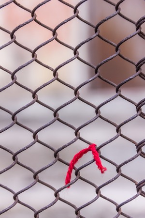 Rusty steel chain link or wire mesh as boundary wall. Red thread. There is still concrete block wall behind the mesh. Best securityの写真素材