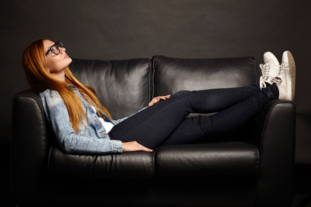 Attractive young woman in glasses sitting on black sofa on black backgroundの写真素材