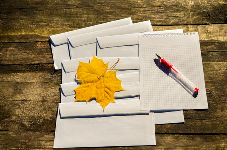 Autumn banner with yellow maple leaf on the mail envelope on a wooden background and white sheet for...
