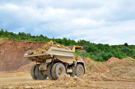 Big yellow dump truck working in the limestone open-pit. Loading and transportation of minerals in...