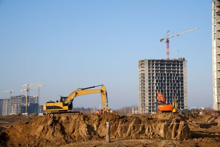 Excavator at a construction site on a background of a construction cranes and building. Backhoe dig...