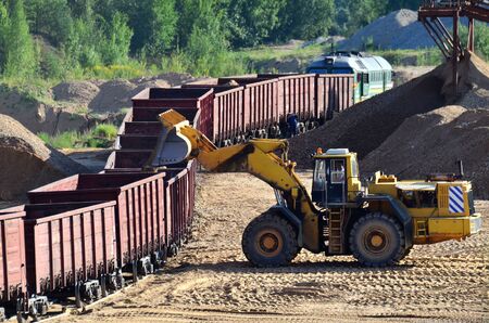 Large heavy front-end loader loading sand it to the freight train. Heavy mining work in a quarry. All-wheel bulldozer for mechanization of loading, digging and excavation operations in open pit.の写真素材