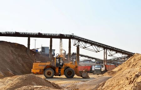Wheel front-end loader unloading sand into heavy dump truck. Crushing factory, machines and equipment for crushing, grinding stone, sorting sand and bulk materialsの写真素材