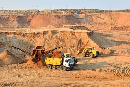 Wheel front-end loader loads sand into a dump truck. Heavy machinery in the mining quarry,...