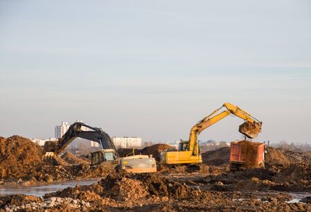 Excavators at a construction site dig the ground for the foundation, laying storm sewer pipes. Road...