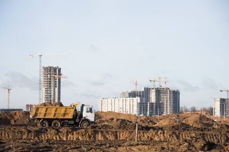Heavy dump trucks and hydraulic luffing jib tower cranes works at a construction site. Tower crane constructing a new residential build. Group of tower cranes builds residential buildings in the cityの写真素材