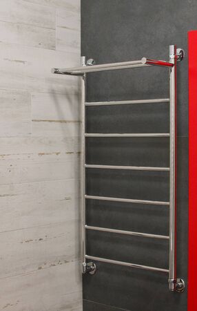 Modern chrome heated towel rail hanging on gray ceramic tiled in the bathroom wall. Luxury light...