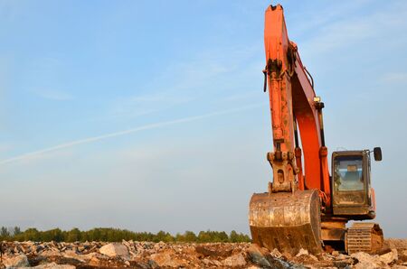 Excavator with a large iron bucket breaks asphalt on a construction site. Demolition work concrete,...