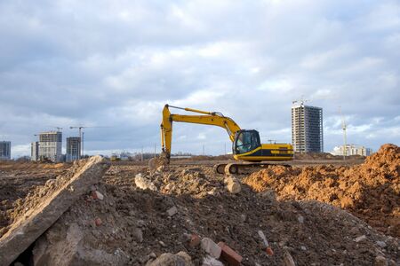 Yellow Excavator at building under construction. Backhoe digs the ground for the foundation and for...