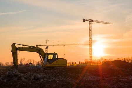 Excavator and tower crane at construction site on sunset background. Construction crane constructing...