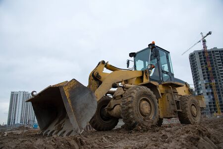 Front-end loader working at construction site. Earth-moving heavy equipment for road work. Public...