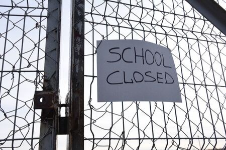 SCHOOL CLOSED text on the yellow plate on a mesh wire fence. Quarantine Area. Students out of schools or universities because of outbreak COVID-19 pandemicの写真素材